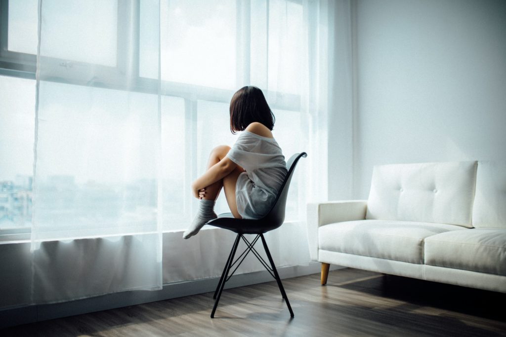 Une personne vue de dos devant des rideaux, sur une chaise.