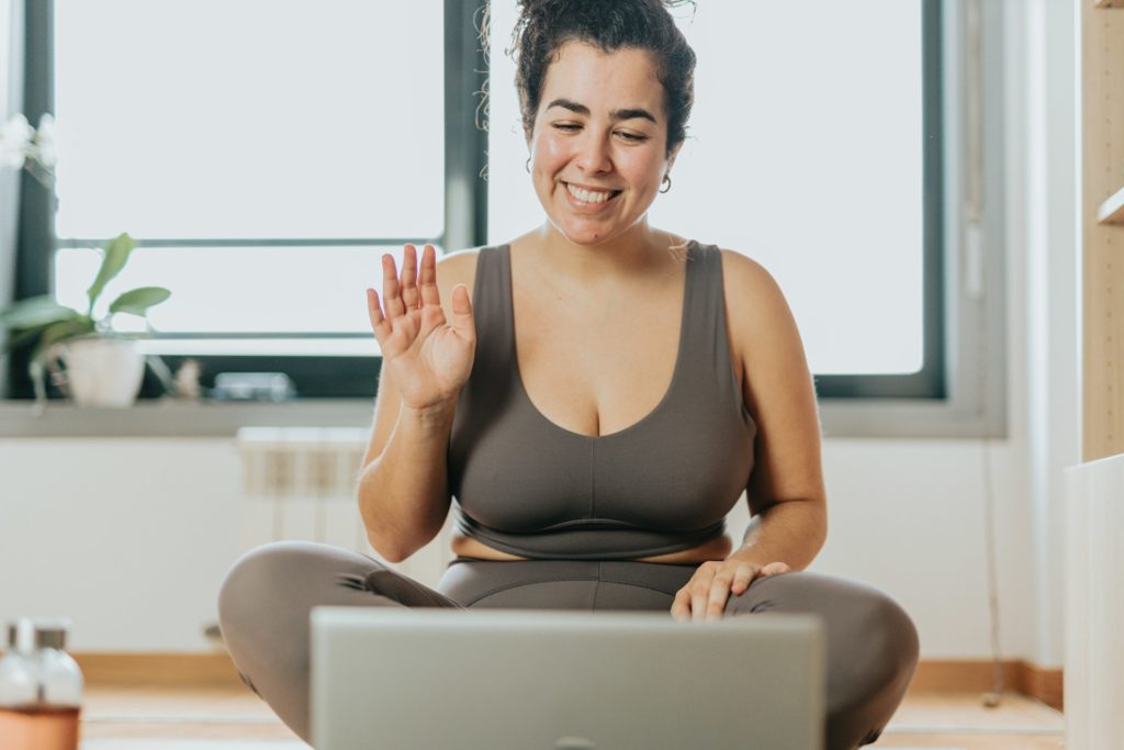 Une sportive démarre une séance de yoga en ligne en saluant son professeur.