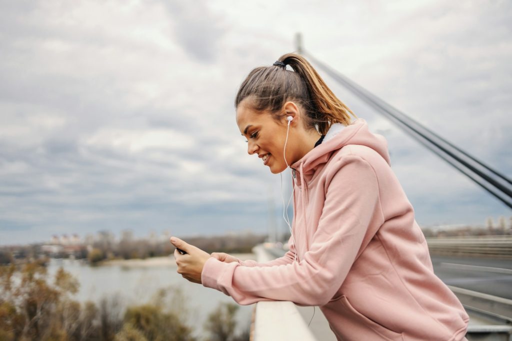 Une sportive vêtue de rose dans une ville regarde son téléphone.