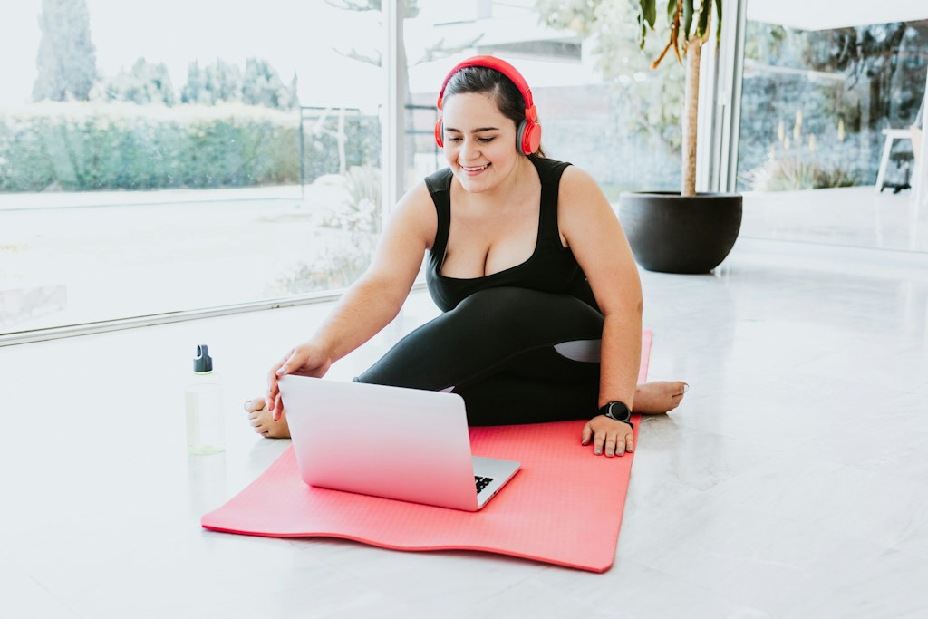 Une personne sourie sur un tapis de yoga avec un labtop.