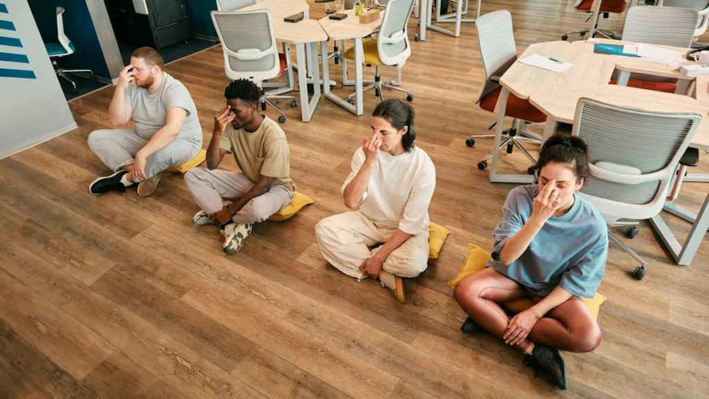 Des salariés assis au sol font une séance de relaxation ensemble au travail.