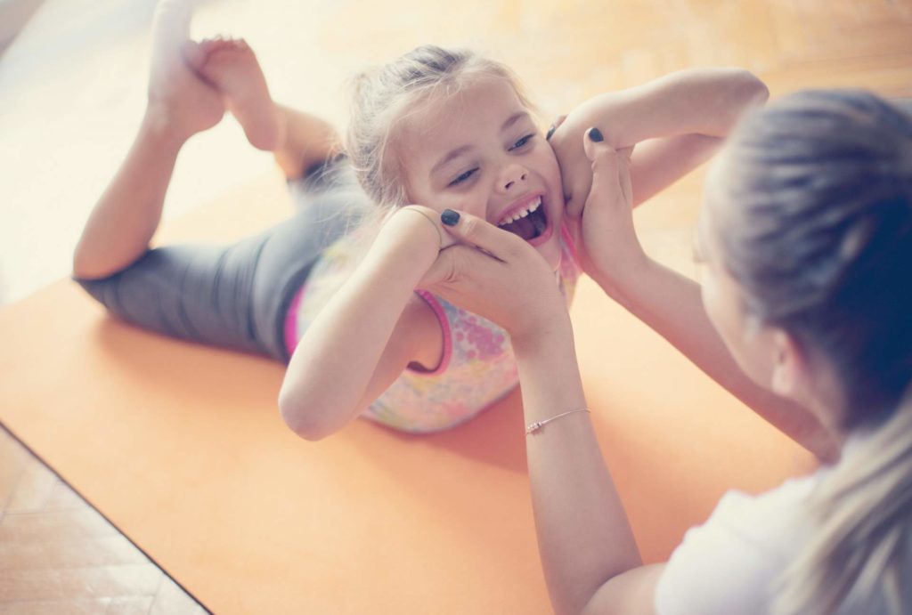Une petite fille sourit avec sa mère sur un tapis de gym.