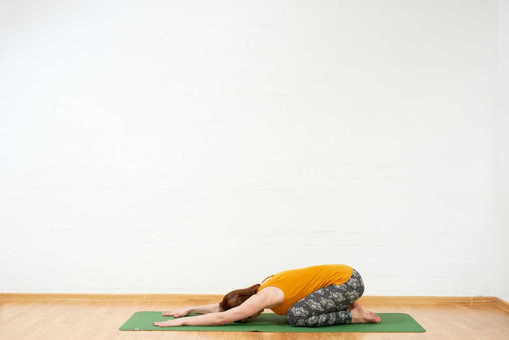 Une pratiquante de yoga s'étire au sol dans une pièce éclairée.