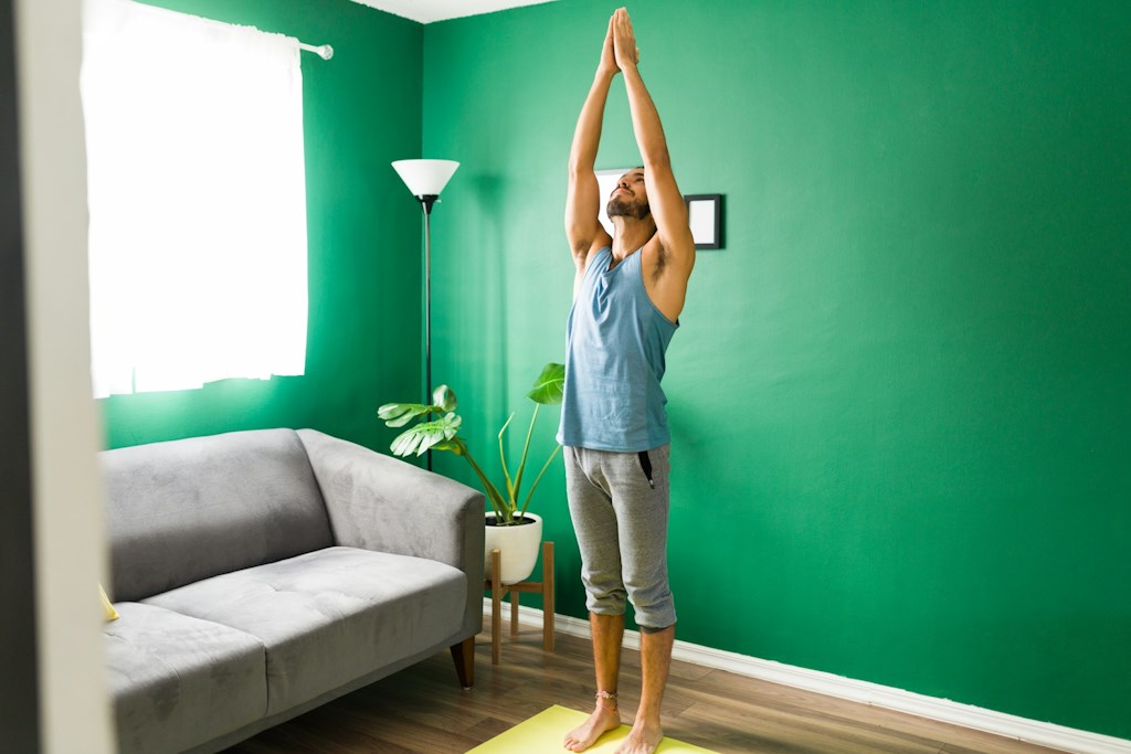 Un jeune lève les mains au plafond dans une maison avec les jambes tendues au sol.