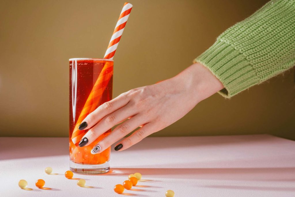 Une femme tient un récipient de couleur rouge avec une paille dedans.