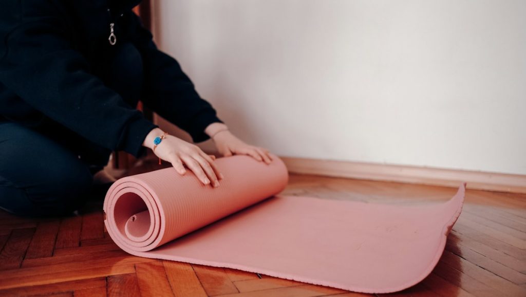 Une personne déroule ou enroule un tapis de gym rose au sol.