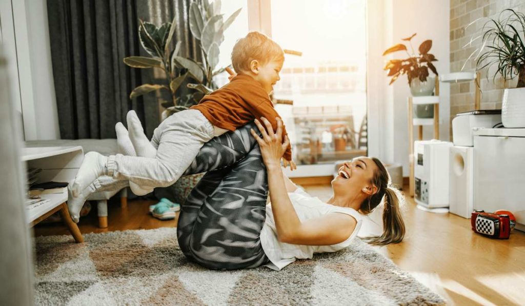 Une maman en position d'abdominaux sur le dos avec son enfant sur les jambes.