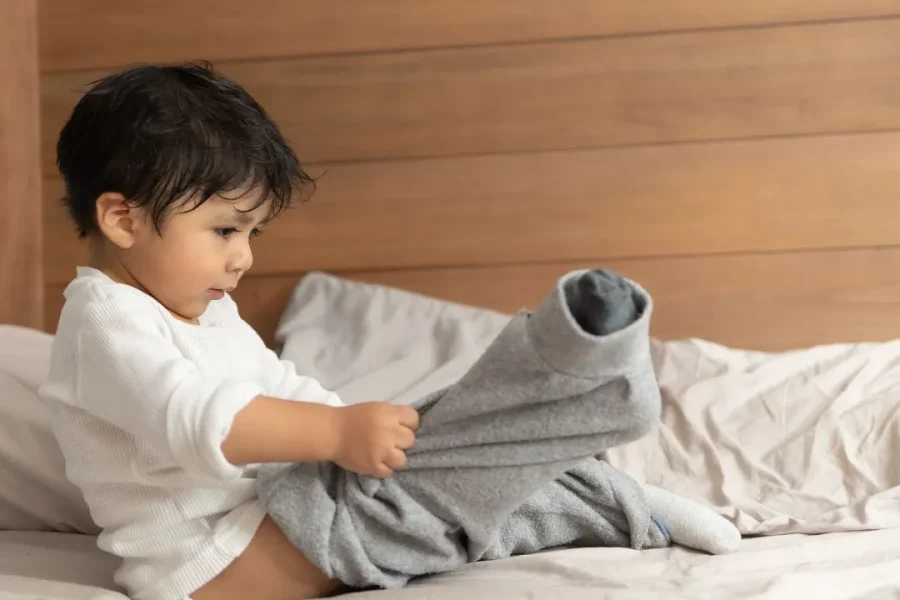 Un jeune petit garçon enfile son pantalon tout seul.