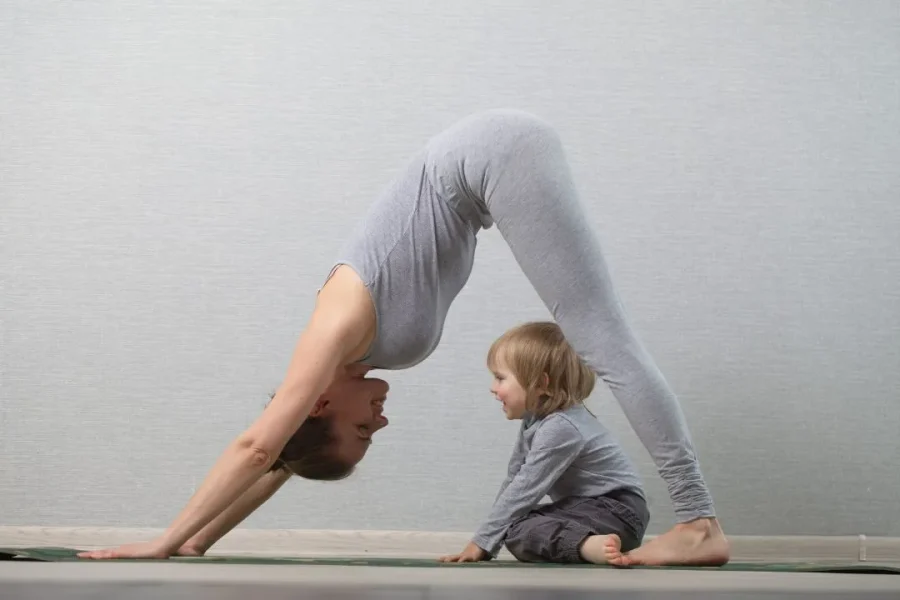 Une maman fait du yoga avec son enfant entre les jambes.