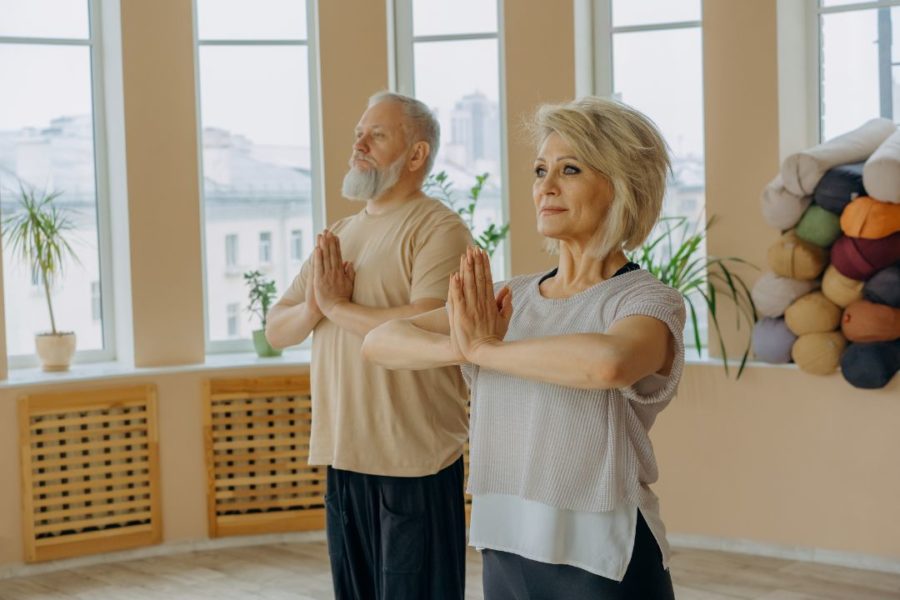 Deux pratiquants de yoga se tiennent debout côte à côte, les mains jointes.