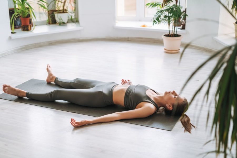 Une femme allongé au sol, étendue sur un tapis, fait une pose de relaxation.