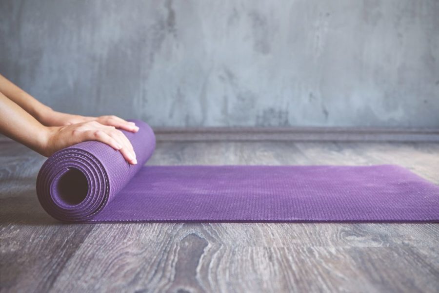 Une femme déroule un tapis pour commencer une séance de yoga.