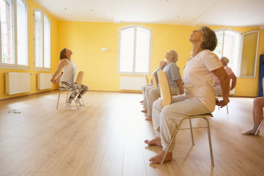 Séniors réalisant une extension dorsale assise pendant un cours de yoga sur chaise.