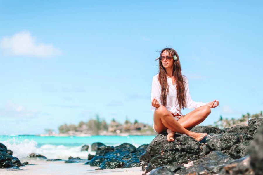 Femme méditant en posture assise sur des rochers face à la mer.