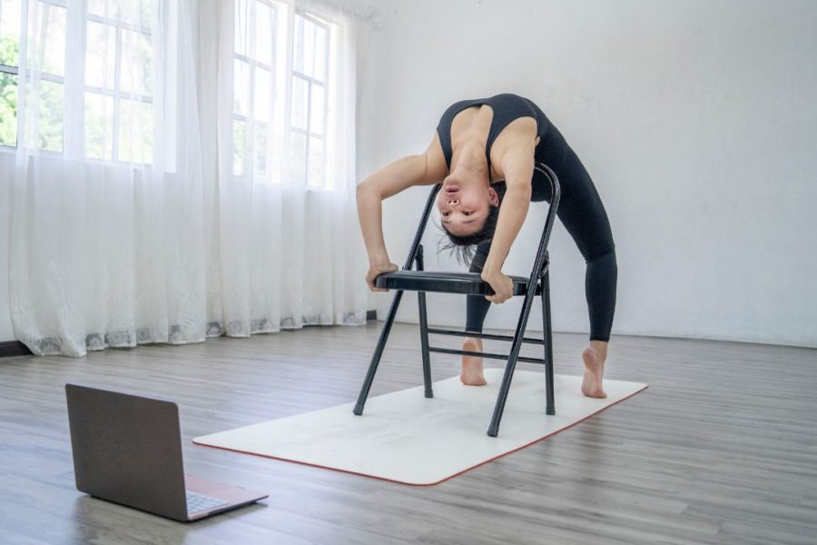 Femme exécutant une posture de yoga en appui sur une chaise pliante.